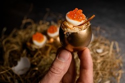 Male hand gently holds beautiful tasty egg stuffed with red caviar and serving in golden shell