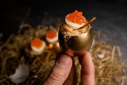 Male hand carefully holds beautiful tasty egg stuffed with red caviar and serving in golden shell