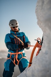 Focus on professional mountaineering ice axe in the ice. Man climber with equipment and ropes on the slope at background