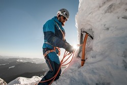 side view of ice axe and man climber with equipment and ropes on the slope against backdrop of sky