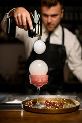 hand of male bartender holds flavour blaster and decorate a glass with cocktail by bubbles with smoke