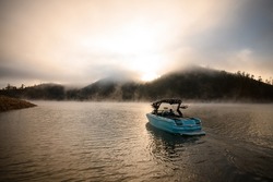 Great view on bright blue modern motor boat floating on water. Scenic view of hills and sky with cumulus clouds on the background