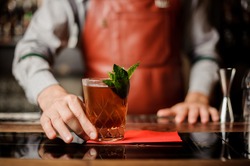 Barman holds a cocktail with mint in his hand. No face. Selective focus
