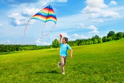 Little boy in blue shirt running with kite in the field on summer day in the park