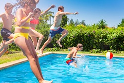 Boys and girls in a group jump in water pool outside during summer vacation