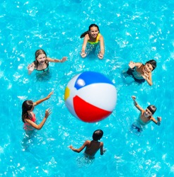 Group of little children in pool stand in circle lift hands up and play volleyball