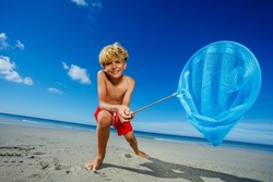 Low angle portrait young boy stand with butterfly nets lean catching critters on the sand ocean beach during tide