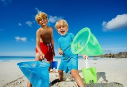 Two happy boys, brothers stand with butterfly nets catching critters on the sand ocean beach during low tide on vacations
