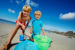 Two smiling happy boys, brothers stand with butterfly nets catching critters on the sand ocean beach during low tide