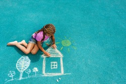 Nice looking black girl drawing house sun and trees with chalk on playground 