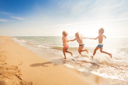 Kids holding hands and running along sandy beach