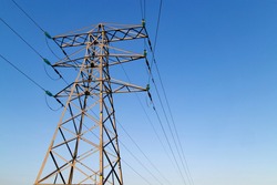 Transmission tower, or power line, in front of a clear blue sky, on a sunny day. These are scattered throughout the UK, so that people can make landline phone calls to others, via a wired connection.