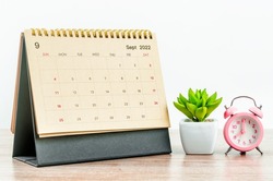 September 2022 green Desk calendar with pink alarm clock on wooden table.