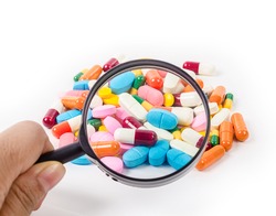Hand holding magnifying glass with medicine pills on white background.
