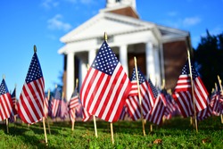 Many miniature US flags set on the grass in front of a memorial chapel close up at a low angle with chapel in the backgraound