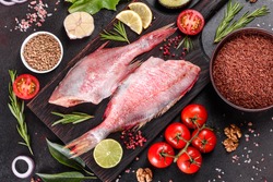 Raw fillet of red sea perch prepared for baking with spices and herbs on a dark background