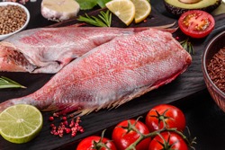 Raw fillet of red sea perch prepared for baking with spices and herbs on a dark background