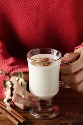 Young women in a red sweater holding a glass with a winter fall drink of kefir and cinnamon.