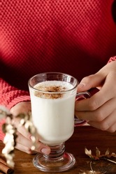 Young women in a red sweater holding a glass with a winter fall drink of kefir and cinnamon.