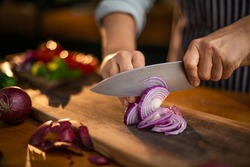 Female chef is precisely slicing red onions on a wooden cutting board in a restaurant. 