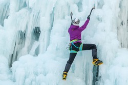 Woman with ice climbing axe hiking at a frozen waterfall