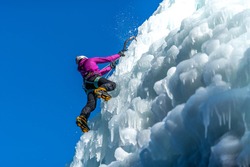  Silhouette of a woman with ice climbing equipment, hiking at a frozen waterfall, swinging the ice axe