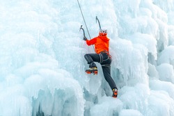 Caucasian man with climbing equipment, ice axes and rope, hiking at a frozen waterfall