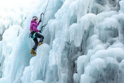 Silhouette of a woman with ice climbing equipment, axe and climbing rope, hiking at a frozen waterfall