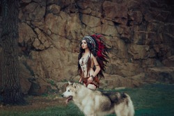 Native American Indian woman. A huntress with a wolf walks through the canyon, among the rocks. The girl has ethnic decorations. The Great, big dog Alaskan Malamute.