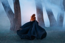 black widow long dark silk fly fabric dress, scary horror woman red hair runs mystery forest turned away black lady night walk gothic blue fog nature tree. art photo shoot mysterious woman silhouette