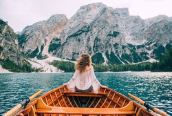Silhouette back woman long hair flying fluttering wind, turned away face sitting in wooden boat. Tourist white blouse long sleeves enjoy nature Italian mountains alpine lake. river waves green forest