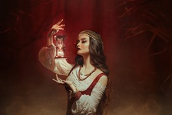 Fantasy woman creates magic. Gypsy girl witch holding magical hourglass in hands. Photo levitation.