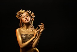 Fantasy portrait of woman, golden skin body. Girl goddess in wreath, gold roses, dress. Beautiful face steel glitter art makeup. Artistic photo dark black background. Girl princess. Fashion model pose