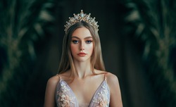 Portrait of fantasy medieval girl princess in dark gothic room. Woman queen looking at camera, beauty face. Vintage trendy glamour dress golden luxury crown, long loose blonde hair. Fashion model.
