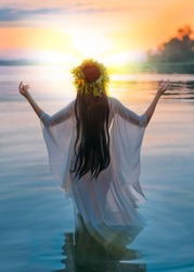 ivan kupala. silhouette happy fantasy vintage woman standing in water hands raised to sky. Slavic girl herbal wreath, long hair white wet dress pagan ritual praying to sun. river sunset Back rear view