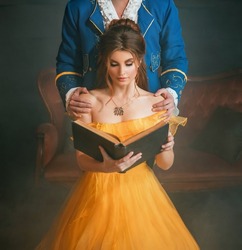 Woman princess holding a book without title cover design reads the text. Fantasy man enchanted prince hugging a beautiful lady by shoulders. Girl in yellow medieval historical dress vintage gown