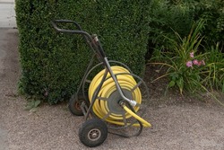 Yellow Hose Pipe  Coiled up on a Rusty Metal Trolley or Cart with a Watering Lance on a Footpath in a Country Cottage Garden in Rural Devon, England, UK