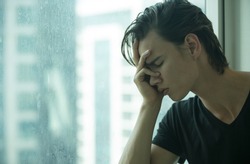 Depression and sad young man by the window with hand on face. 