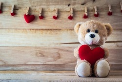 Teddy bear holding a heart-shaped pillow with plank wood board background