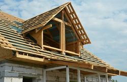 An unfinished attic roofing construction. Roof framing of an attic with vapor barrier, roof beams, trusses, rafters and braces. 