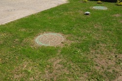 Two manhole covers on the green lawn of a septic tank system, sewer with a vent pipe installed in the ground. A septic tank in the ground in the backyards of the house. 