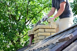 Repairing and rebuilding a brick chimney. A building contractor is rebuidling a chimney on a house with asbestos roof.