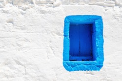 Iconic blue wooden window on white stone wall of typical Greek house, Greece