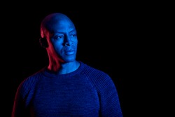 African American man with blue and red light, isolated on black background, looking sideways. Copyspace.