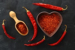 red hot chili peppers powder in heart shaped bowl on black stone table. Love concept. Top view flat lay with copy space