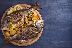 Roasted fish and potatoes, served on wooden tray. overhead, horizontal, copy space - image