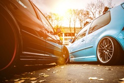 Two modified low cars in brown and light blue color. Stance custom cars with a forged polished wheels parked on a street at sunny day. Tuned automobiles