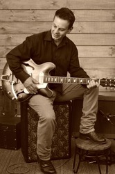 A guitarist plays a hollow body electric guitar in studio recording session. Candid classic sepia tone and colour.