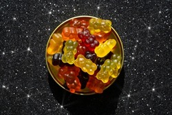 Assortment of gummy bears in a round ting box on a glittering black background