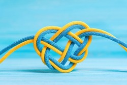 Heart shaped celtic knot made from braided cords painted the colors of the national flag of Ukraine on blue background. Creative unity, faith and protection concept.
